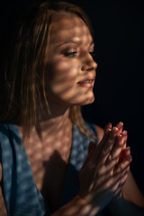 Beautiful woman confesses in the confessional. Praying woman, fine art portrait with interesting ligth and shadow pattern. Absolution.