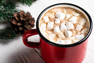 Obraz na płótnie Canvas Close up view of red cup of cocoa with marshmallows and cinnamon near pine cone