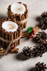 Scented candles decorated with cinnamon sticks near red beads and pine cones