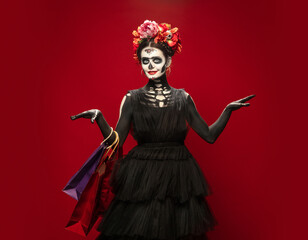 Fototapeta premium Shopping. Young girl like Santa Muerte Saint death or Sugar skull with bright make-up. Portrait isolated on red studio background with copyspace. Celebrating Halloween or Day of the dead. Black friday
