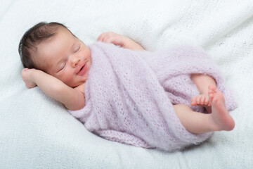 New born baby girl sleeps at home and smiling in a dream. Cute little kid's portrait