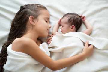 Obraz na płótnie Canvas Little girl sleeps with her new born baby sister at home. Cute children's portrait