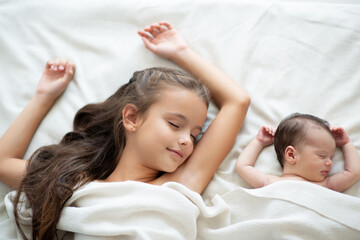 Obraz na płótnie Canvas Little girl sleeps with her new born baby sister at home. Cute children's portrait