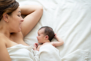 Happy smiling mother lying in bed with her newborn daughter at home, takes care about baby. Family values, mothercare