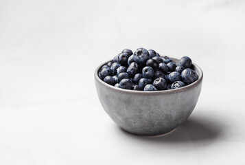 Bowl of fresh ripe blueberries on a white marble background. Healthy seasonal fruit. Organic food blueberries for healthy lifestyle and eating. Vegan, vegetarian concept. Rustic.