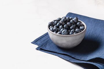 Fototapeta na wymiar Bowl of fresh ripe blueberries on a blue fabric and white marble background. Healthy seasonal fruit. Organic food blueberries for healthy lifestyle and eating. Vegan, vegetarian concept. Rustic.
