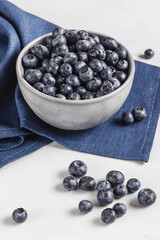 Bowl of fresh ripe blueberries on a blue fabric and white marble background. Healthy seasonal fruit. Organic food blueberries for healthy lifestyle and eating. Vegan, vegetarian concept. Rustic.