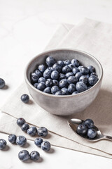 Bowl of fresh ripe blueberries on a white fabric and white marble background. Healthy seasonal fruit. Organic food blueberries for healthy lifestyle and eating. Vegan, vegetarian concept. Rustic.