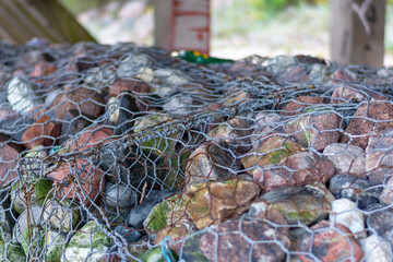 Fototapeta na wymiar Natural stones fixed with a metal net to strengthen the coast. Close-up, selective focus
