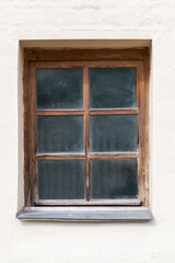 Old dusty window with wooden frame in a white wall