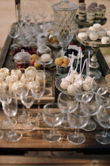 Wedding buffet and decorations. Sweets, cookies, berries and fruits. Macaroons. Wooden cart on grass. Nature. Pastel colors. Dishes and serving. Catering
