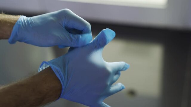 Protection against contagious disease, coronavirus, man wearing hygienic gloves to prevent infection. Media. Close up of man hands putting on protective blue latex gloves.