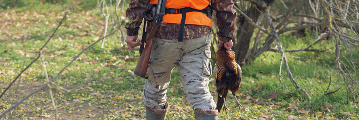 A man with a gun in his hands and an orange vest on a pheasant hunt in a wooded area in cloudy...