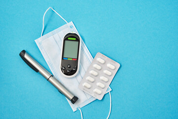 face mask, glucose meter and syringe pen for injection of insulin on a blue background, top view copy space