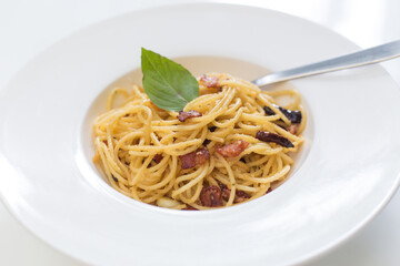 Stir fried spaghetti with dried chilli and crispy bacon  in a white dish.
