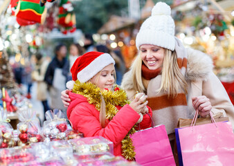 Cheerful little girl looking for decorations on Christmas street market while shopping with her mother
