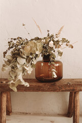 Beautiful autumn bouquet of dried flowers of brown shades in a glass vase on a beige background