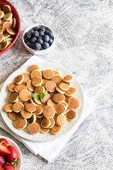 Fototapeta na wymiar Tiny pancakes for breakfast. Cereal pancakes with blueberries, bananas, strawberries. Trendy food. 