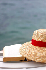 Open book and straw hat by the water. Selective focus.