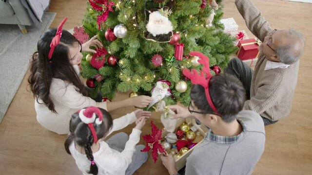 Top view of Merry christmas asian family prepare and decorate x'mas tree together in living room at home. Happy cheerful asian family enjoy in quarantine activity time concept.