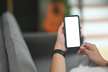 Cropped shot of hands holding smartphone with blank screen on comfortable couch.