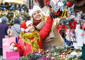 Smiling cute preteen girl having fun on Christmas fair with mother, selecting decoration for home