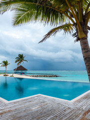 View on a infinite pool with a woodn deck and palm trees on a white sand beach of Indian ocean on a luxury resort hotel on Maldive islands