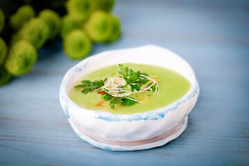 Homemade cream soup with green peas, parsley leaves and alfalfa sprouts on a blue wooden background
