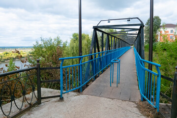 Bridge over the abyss with blue railing, metal construction. The narrow blue iron bridge surrounded by greenery.