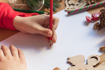 Obraz premium Children's hand writes with a pencil. Child's hands, the sheet of paper, pencils and Christmas decorations on a wooden surface. Concept of New year and Christmas. Side view