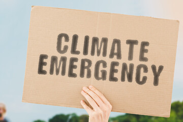 The phrase " Climate emergency " on a banner in men's hand with blurred background. Global warming. Pollution. Humanity. Earth. Industry. Dangerous