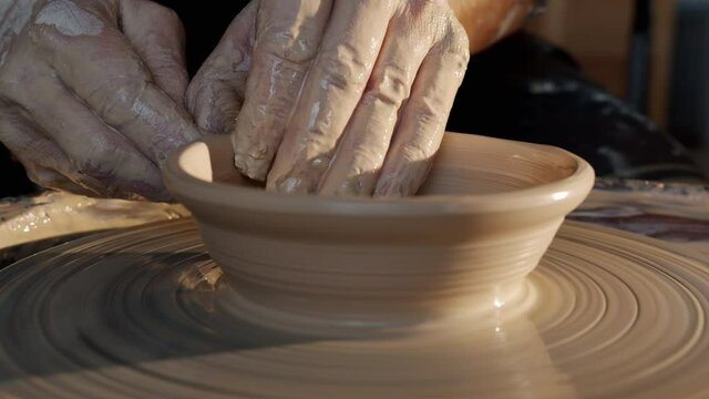 Close-up of bowl spinning on throwing-wheel and potter' hands shaping clay in workshop. Beautiful hand-made artworks and creative people concept.