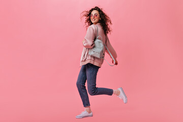Fototapeta na wymiar Stylish woman in jeans and jacket moving on pink background