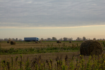 Cargo transportation by trailers. The trailer drives along the highway among autumn fields and bales of hay.