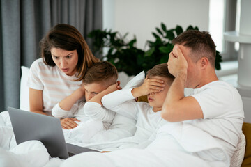 Beautiful parents with kids enjoying at home. Young family watching movie on lap top
