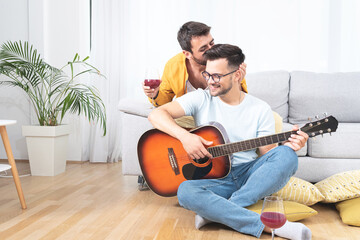 Young man playing guitar as boyfriend kisses him on head