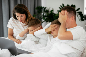 Beautiful parents with kids enjoying at home. Young family watching movie on lap top