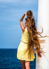 Fototapeta na wymiar Sexy long hair model in yellow dress, standing with the back, one hand fixing the wild hair
