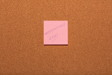 Vaccination 2021? handwritten on a pink sticker on a cork notice-board.