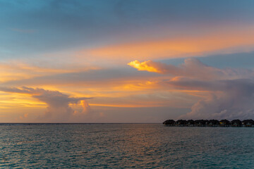 Obraz na płótnie Canvas Scenic view on small villas on horizon under colorful clouds in sky during sunset in Indian ocean on maldive islands