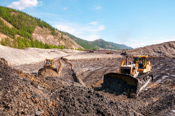 Open pit mining (natural gold) in mountainous areas. A bulldozer collects a pile of mountain soil. Then, wheel loaders transport this mountain soil and dump it into industrial washing equipment in ord