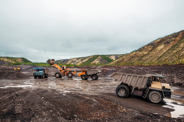 Obraz premium Loading of mountain soil into the body of a mining dump truck using a wheel loader, and further transportation of the cargo. Extraction of minerals in the mountainous region of Eastern Siberia