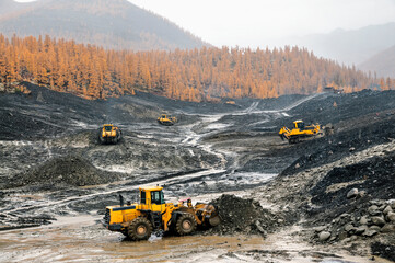 Open pit mining (natural gold) in mountainous areas. A bulldozer collects a pile of mountain soil. Then, wheel loaders transport this mountain soil and dump it into industrial washing equipment in ord