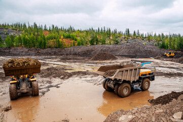 Loading of mountain soil into the body of a mining dump truck using a wheel loader, and further transportation of the cargo. Extraction of minerals in the mountainous region of Eastern Siberia © Letopisec