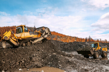 Open pit mining (natural gold) in mountainous areas. A bulldozer collects a pile of mountain soil. Then, wheel loaders transport this mountain soil and dump it into industrial washing equipment in ord