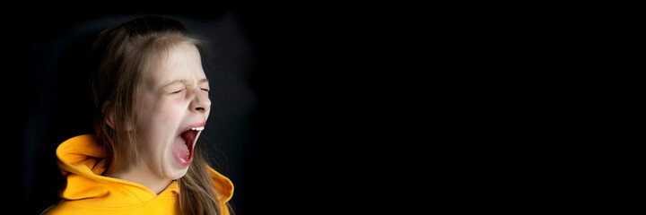 Teenager girl in an orange sweatshirt with bright emotions on her face on a black background. Girl...