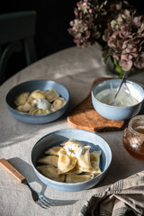 Pyrogy (pierogi) and sour cream in blue plates on round table with linen tablecloth ,