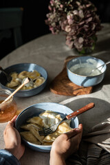 Pyrogy (pierogi) and sour cream in blue plates on round table with linen tablecloth ,