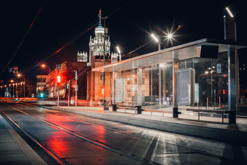 Naklejka premium A modern tram stop in the center of Moscow. Night. No people. Lanterns and city lights are on. A Stalinist skyscraper in the background