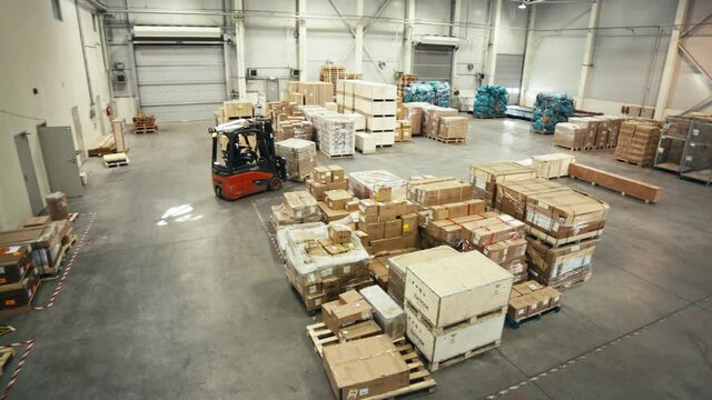 Red forklift driving around modern well arranged warehouse with shipment load. Panning high angle shot.